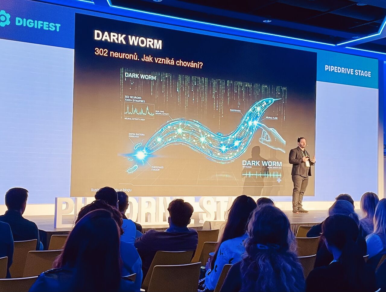 Jan Tyl na Pipedrive Stage představuje DARKWORM; na plátně je ilustrace digitálního červíka a v popředí publikum.